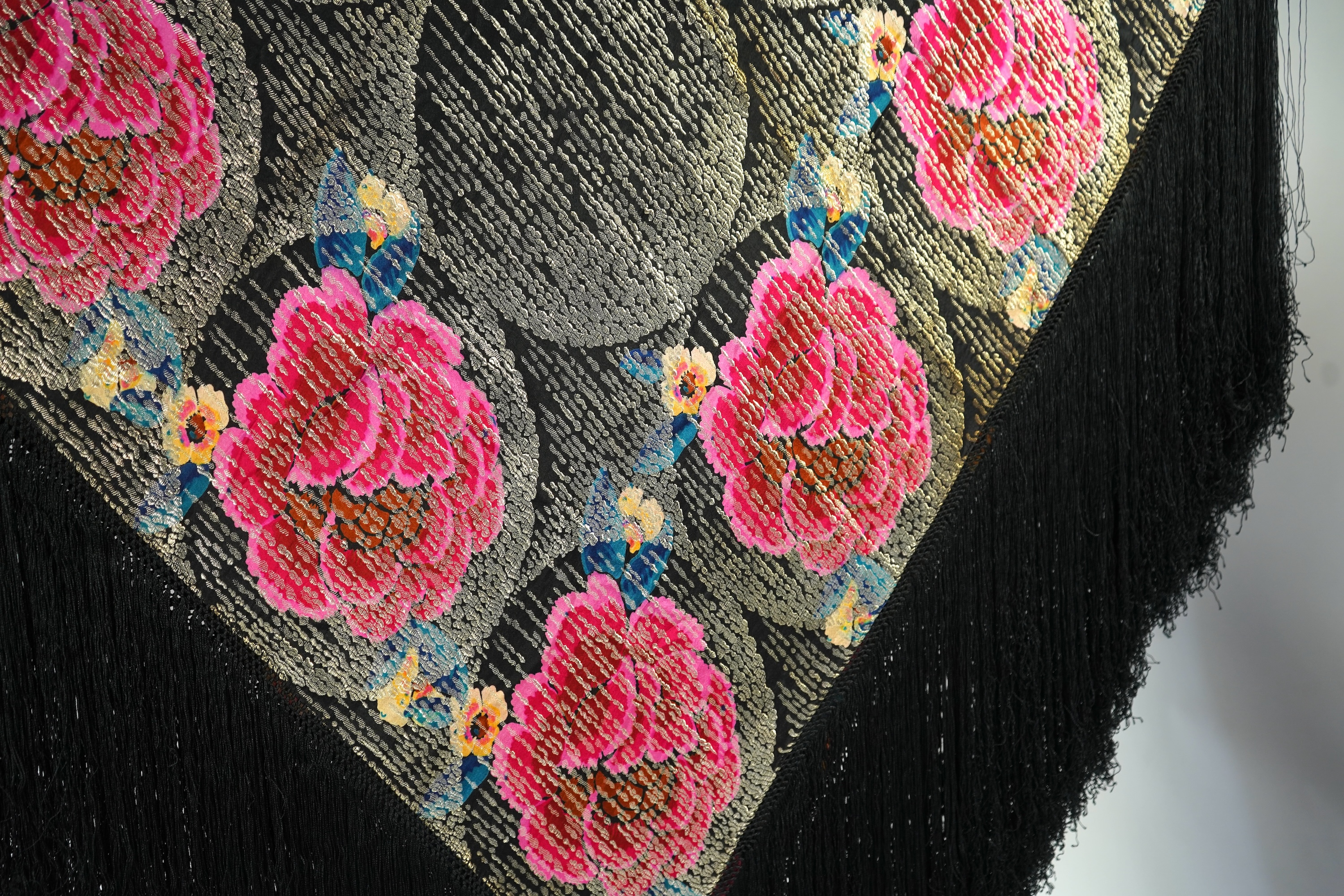 A 1930's ‘jazz age’ black and coloured silk lame evening shawl. Woven with giant pink and red roses and silver thread stripes, edged with long silk fringing. 118cm x 123cm. Condition - colours and silk strong. Fringing g